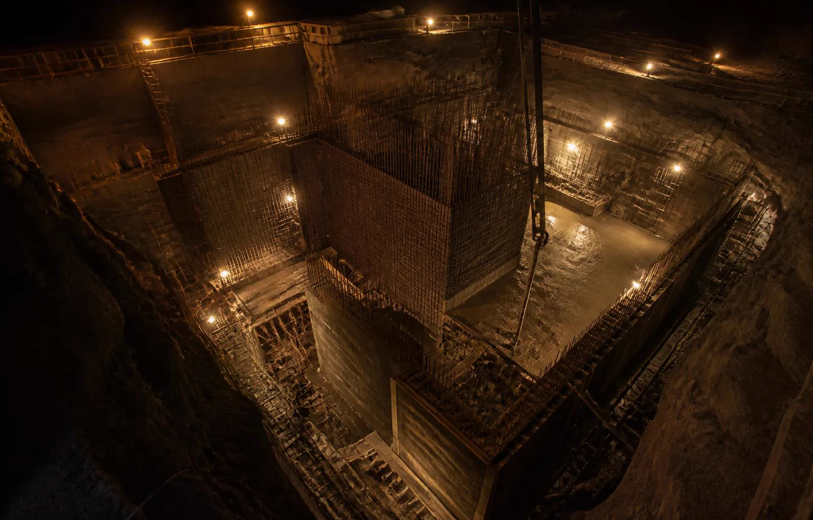 Dunkle Baustelle des privaten Atomschutzbunkers Statum Arcis bei Nacht mit freiliegender Bewehrung, Ortbeton und gedimmtem amberfarbenem Arbeitslicht